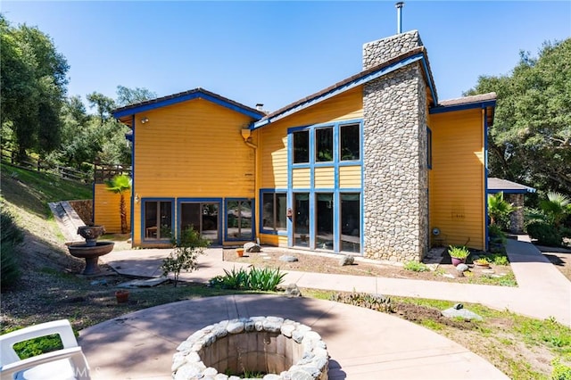 rear view of property featuring a fire pit, a chimney, and a patio
