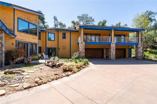 view of front of property featuring stone siding, concrete driveway, a balcony, and a garage