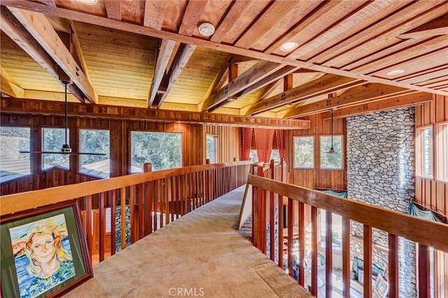 hall with beam ceiling, wooden ceiling, wood walls, and carpet