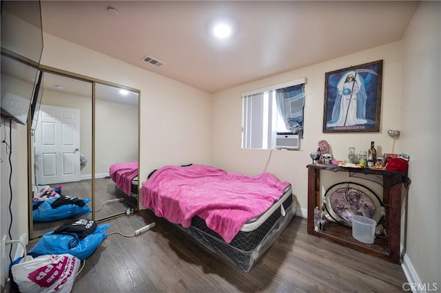 bedroom with visible vents, wood finished floors, cooling unit, a closet, and baseboards