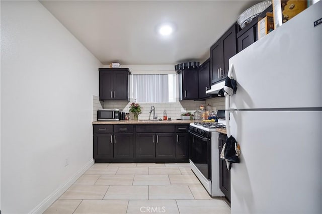 kitchen with stainless steel microwave, under cabinet range hood, gas range oven, freestanding refrigerator, and a sink