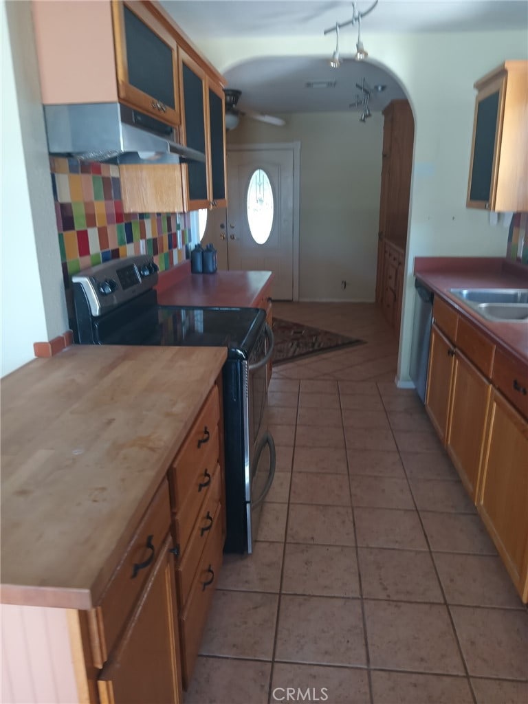 kitchen featuring under cabinet range hood, range with electric stovetop, stainless steel dishwasher, arched walkways, and light tile patterned flooring