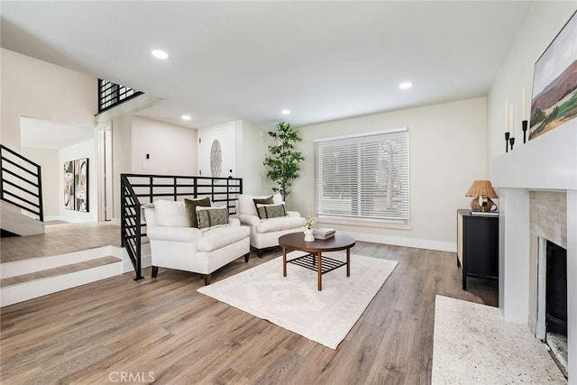 living area with stairway, baseboards, light wood finished floors, a premium fireplace, and recessed lighting