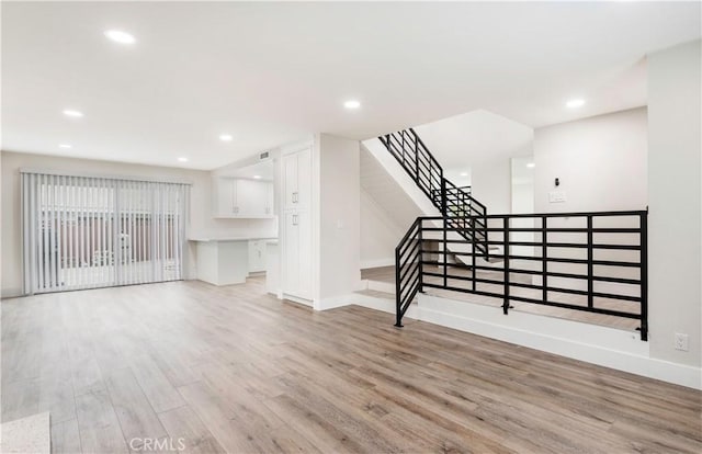 unfurnished living room featuring recessed lighting, stairs, light wood-type flooring, and baseboards