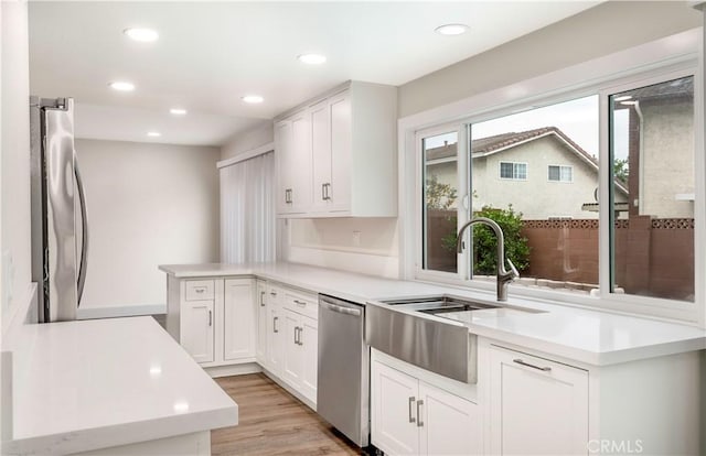 kitchen with a peninsula, light countertops, white cabinets, appliances with stainless steel finishes, and light wood-type flooring