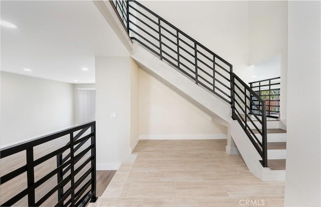 stairway with recessed lighting, wood finished floors, baseboards, and a towering ceiling