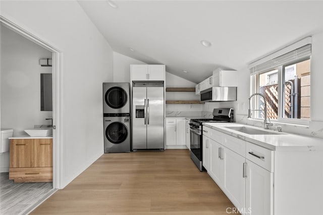 kitchen with open shelves, stainless steel appliances, stacked washer / drying machine, and a sink