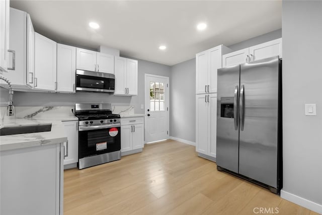 kitchen featuring light wood finished floors, white cabinets, stainless steel appliances, and a sink