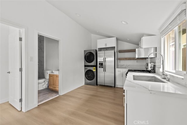 kitchen featuring light wood finished floors, open shelves, a sink, stainless steel refrigerator with ice dispenser, and stacked washer / dryer