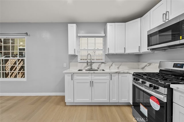 kitchen featuring light wood-style flooring, a sink, appliances with stainless steel finishes, white cabinets, and baseboards