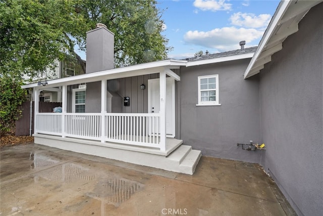 doorway to property featuring stucco siding, covered porch, and a chimney