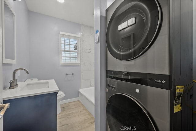 washroom featuring a sink, light wood-style floors, stacked washer / dryer, baseboards, and laundry area