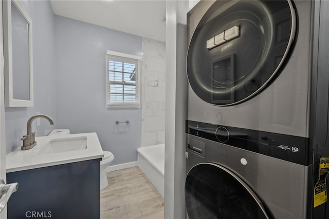 laundry room with baseboards, laundry area, light wood-style flooring, stacked washer / drying machine, and a sink