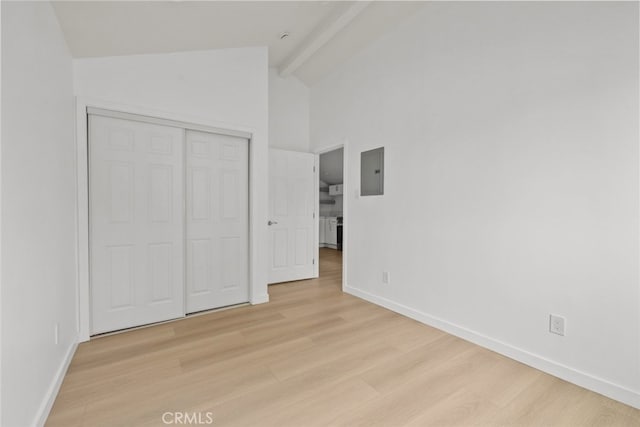 unfurnished bedroom featuring electric panel, beam ceiling, light wood-style flooring, and baseboards