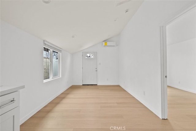 interior space with lofted ceiling, light wood-style flooring, baseboards, and a wall mounted AC