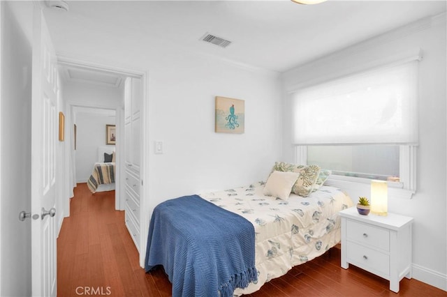 bedroom with visible vents, baseboards, attic access, and wood finished floors