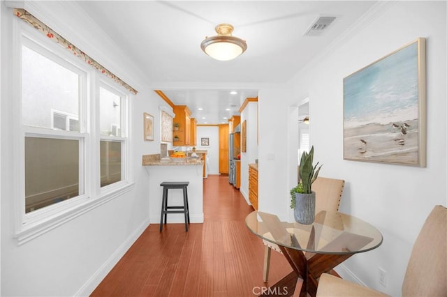 corridor with dark wood finished floors, baseboards, visible vents, and ornamental molding