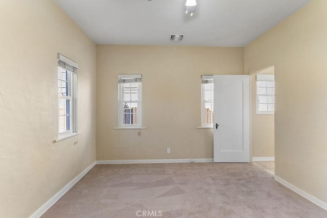 unfurnished room with visible vents, light colored carpet, and baseboards