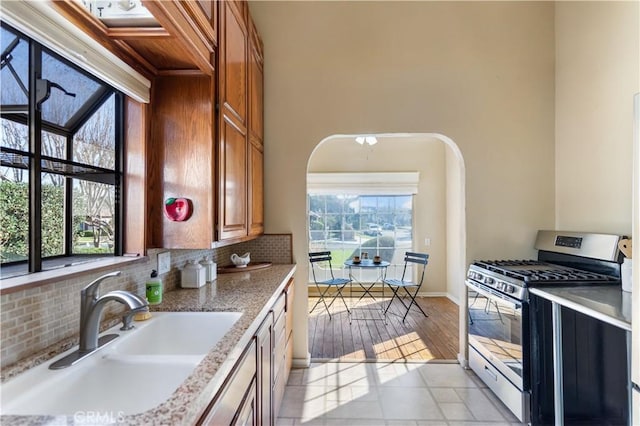 kitchen featuring brown cabinets, a sink, backsplash, gas stove, and arched walkways