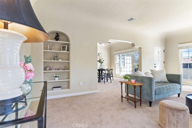 carpeted living area with built in shelves, a healthy amount of sunlight, visible vents, and arched walkways