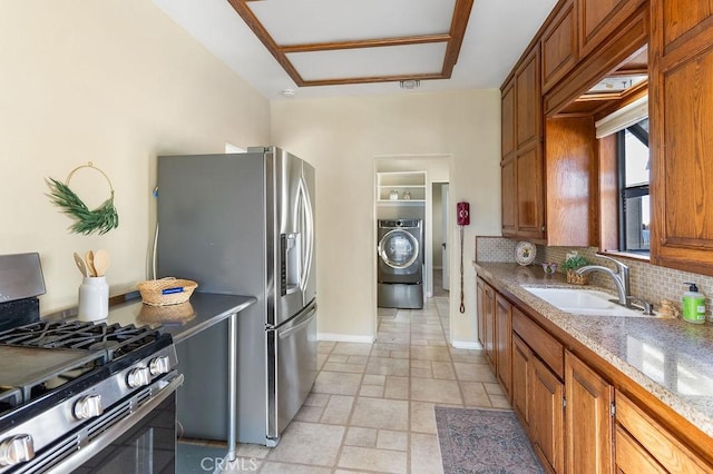 kitchen with tasteful backsplash, appliances with stainless steel finishes, brown cabinetry, washer / clothes dryer, and a sink