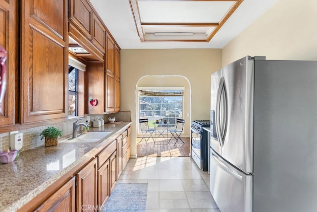 kitchen with brown cabinets, a sink, freestanding refrigerator, range with gas cooktop, and decorative backsplash