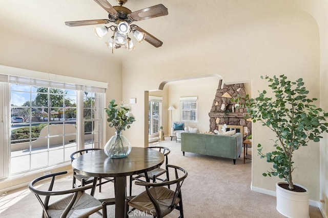 dining area with baseboards, a fireplace, arched walkways, ceiling fan, and light colored carpet