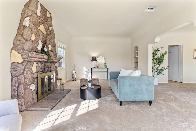 carpeted living area with visible vents, built in shelves, arched walkways, a fireplace, and baseboards