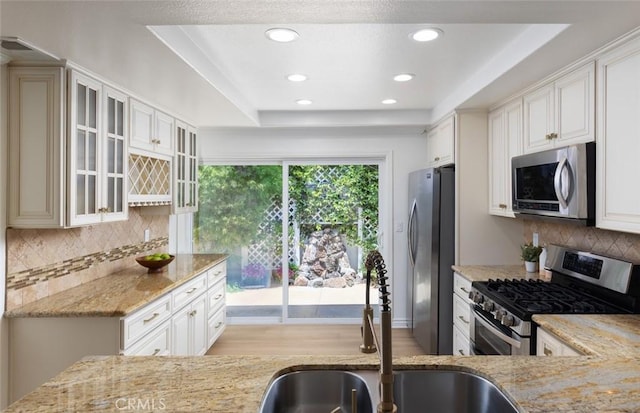 22902 Via Cruz, Laguna Niguel, CA 92677 - kitchen with appliances with stainless steel finishes, a sink, light stone countertops, tasteful backsplash, and glass insert cabinets