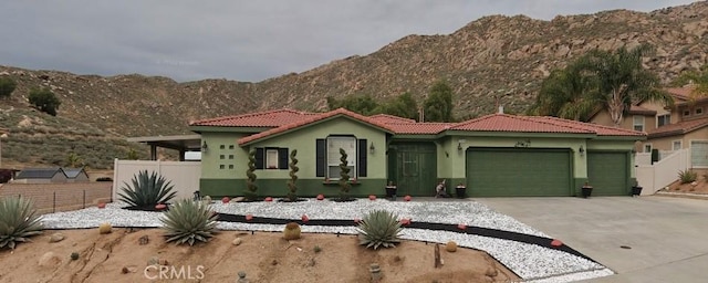 mediterranean / spanish home with a garage, fence, stucco siding, a mountain view, and a tile roof