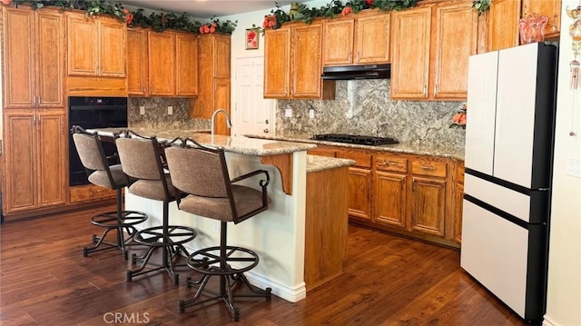 kitchen featuring freestanding refrigerator, brown cabinets, under cabinet range hood, and dark wood finished floors