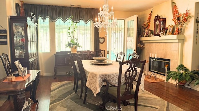 dining room featuring visible vents, a tiled fireplace, wood finished floors, baseboards, and a notable chandelier