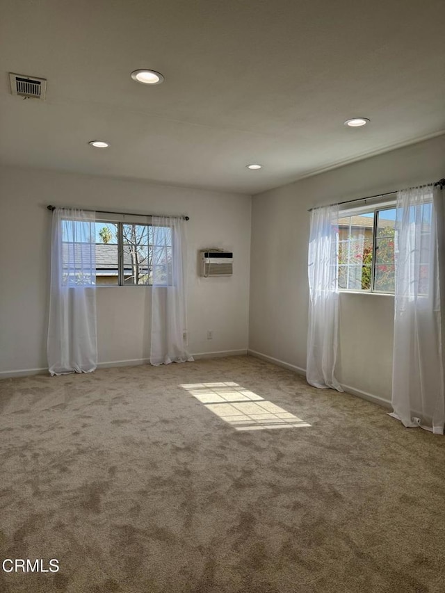 spare room with visible vents, a healthy amount of sunlight, an AC wall unit, and carpet flooring