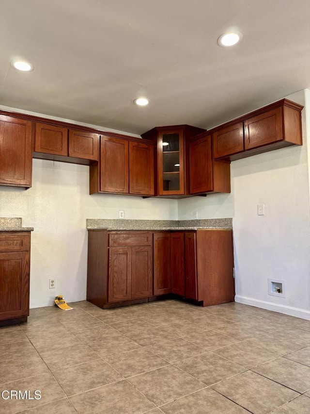 kitchen featuring light stone counters, recessed lighting, glass insert cabinets, and brown cabinets