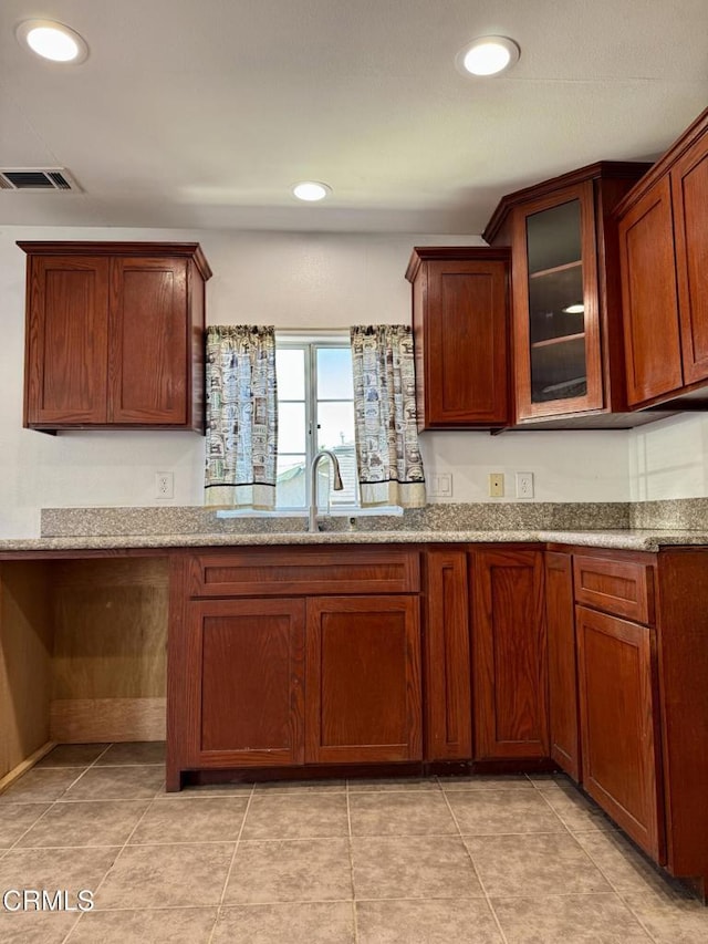 kitchen with a sink, visible vents, light stone countertops, and glass insert cabinets