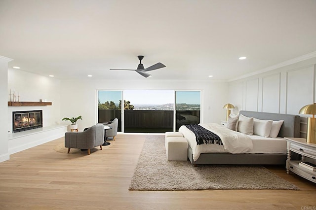 bedroom featuring access to exterior, a decorative wall, a glass covered fireplace, and wood finished floors