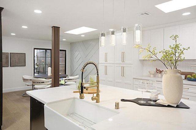 kitchen with wood finished floors, a skylight, a sink, light countertops, and pendant lighting