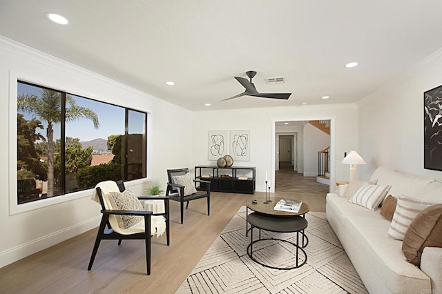 living area with baseboards, visible vents, light wood finished floors, and ornamental molding