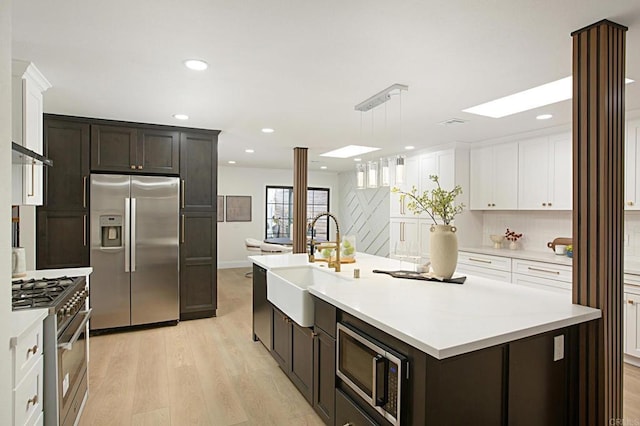 kitchen featuring light wood finished floors, a sink, light countertops, white cabinets, and appliances with stainless steel finishes