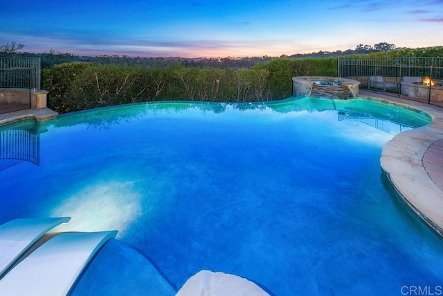 pool at dusk featuring a pool with connected hot tub