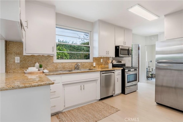 kitchen featuring light stone counters, decorative backsplash, appliances with stainless steel finishes, white cabinetry, and a sink