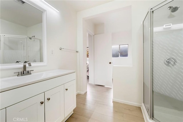 full bath featuring vanity, a shower stall, wood finished floors, and baseboards