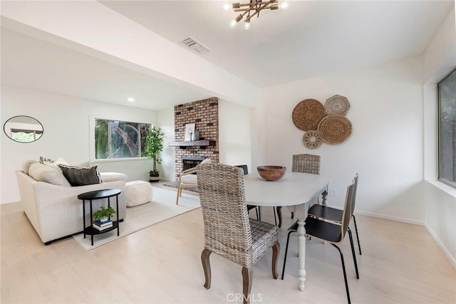 dining area with light wood finished floors, visible vents, a fireplace, and baseboards