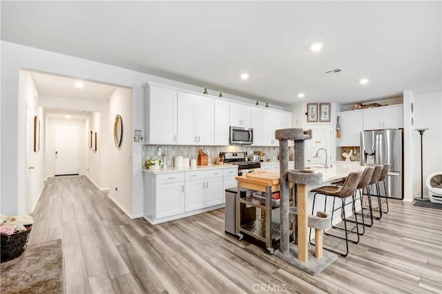 kitchen with visible vents, a breakfast bar, a sink, tasteful backsplash, and appliances with stainless steel finishes