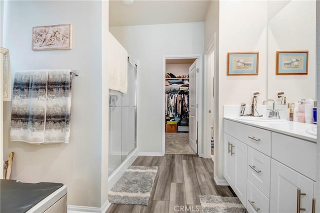 full bath with a walk in closet, wood finished floors, a shower stall, baseboards, and vanity