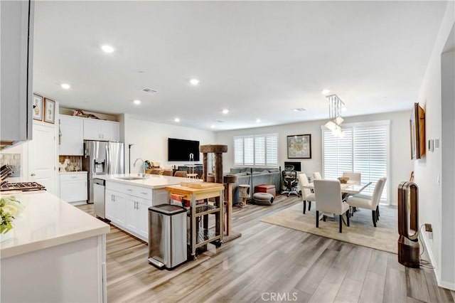 kitchen with light wood finished floors, stainless steel appliances, decorative backsplash, light countertops, and a sink