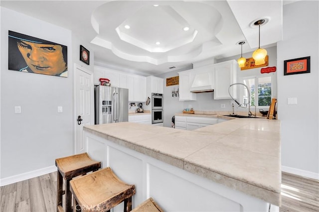 kitchen with white cabinets, a tray ceiling, a breakfast bar, light wood-style floors, and appliances with stainless steel finishes