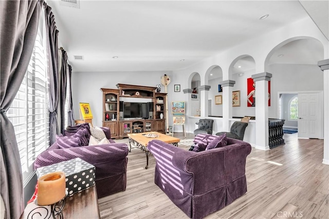 living room with arched walkways, light wood-style floors, recessed lighting, and decorative columns