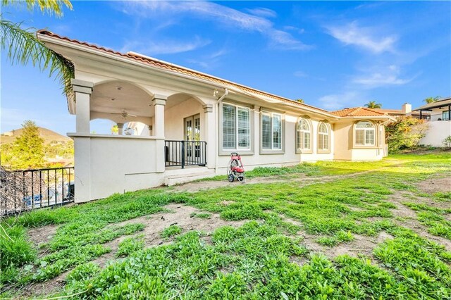 rear view of property featuring stucco siding, a ceiling fan, and fence