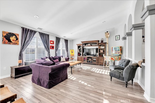 living room with light wood finished floors, arched walkways, vaulted ceiling, baseboards, and visible vents